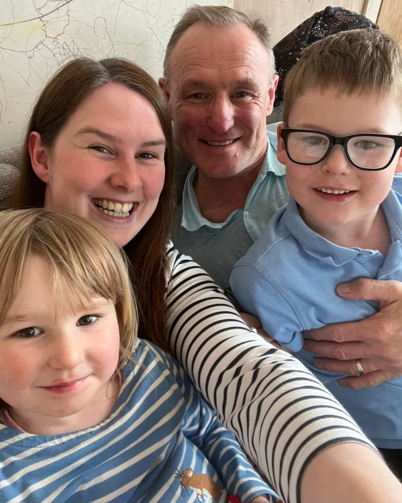 Mum and dad, Louise and Alfie sit on the. sofa with. Eilidh and Ruairidh. They are smiling and sat close to one another.