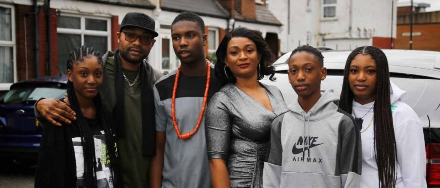 Kelly's family are huddled together posing for a photo on a street. Kelly and his mum, Isoken, are in the middle, with the rest of the family surrounding.