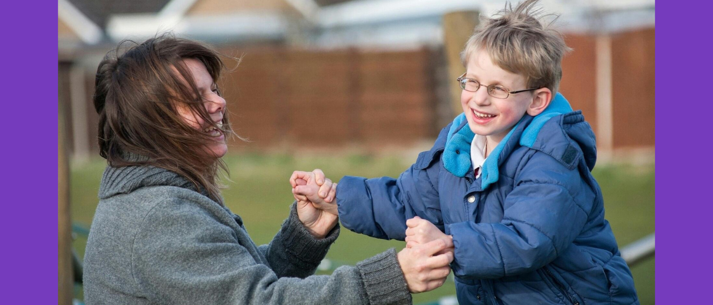 A mum with brown hair is playing outside with her small son wearing a blue coat