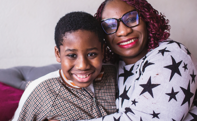 A son and his mother wearing glasses smile, sitting on the sofa together