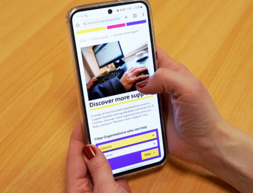 A photo of two hands holding a mobile phone and browsing the Discover more support page on Family Fund website.