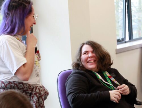 A supported intern sat in an office, next to her is her job coach. They are laughing together