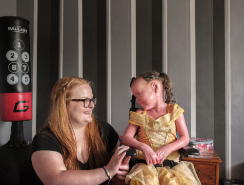 A mum crouched next to her daughter in a wheelchair, looking at each other smiling