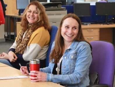 Two colleagues sat at a long desk in an office, smiling