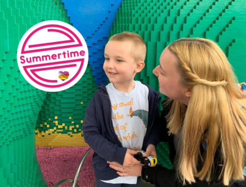 A little boy and his mum kneeling down looking closely at him. In the top left corner is a white circle with pink lines and text says 'Summertime'